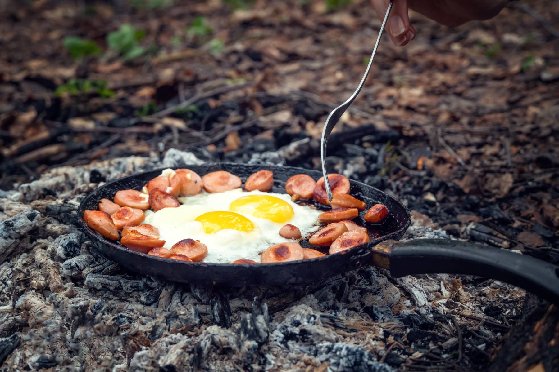Eggs and sausage cooking in a camping frying pan over hot coals