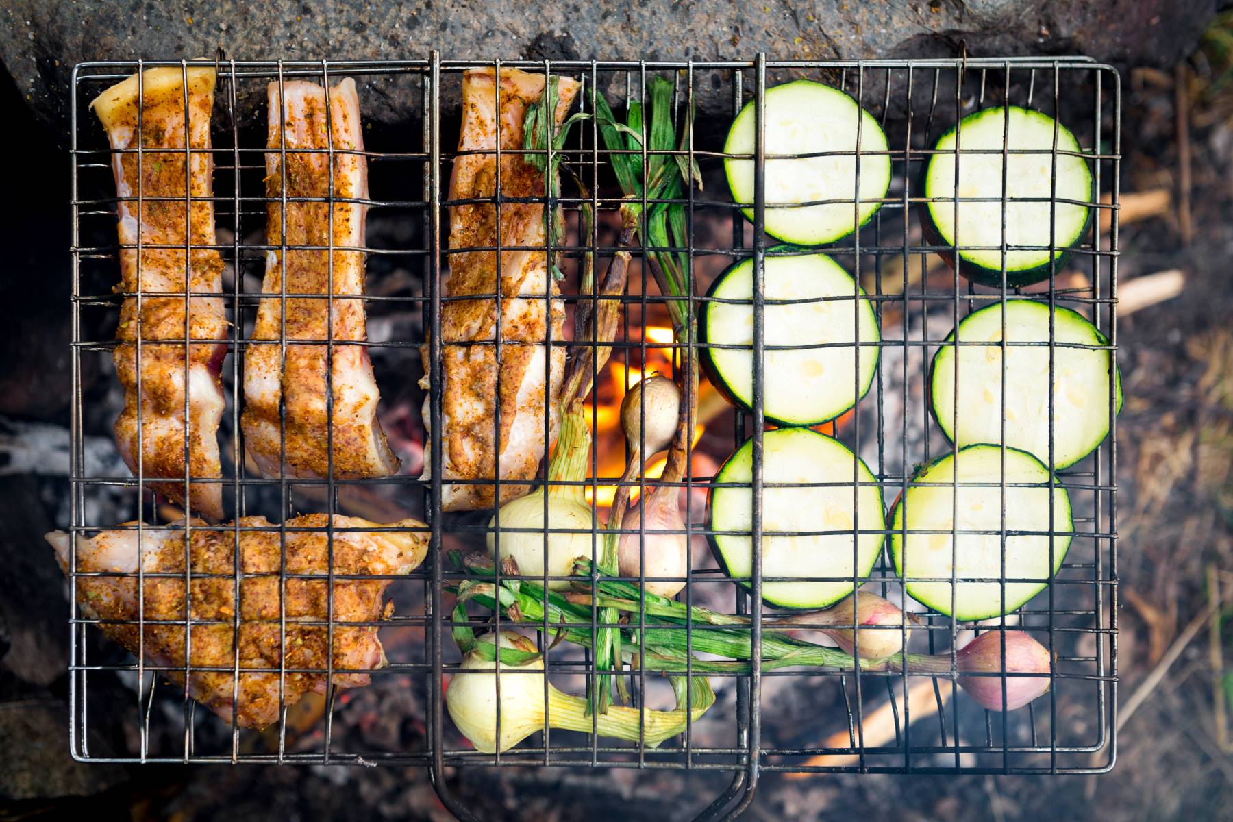 Campfire grilling basket with meat and veggies cooking over an open fire